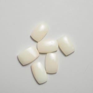 Könnte beinhalten: Sechs weiße, ovale Perlmutt-Cabochons. Die Cabochons sind glatt und haben einen leichten irisierenden Schimmer.