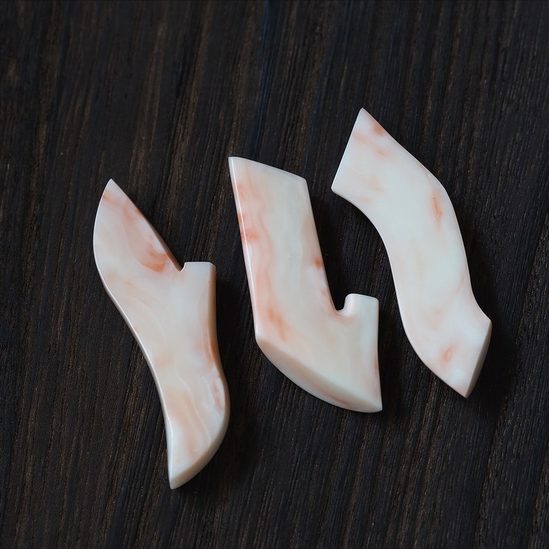 May include: Three white and pink marbled ceramic pieces shaped like abstract shoes. The pieces are arranged in a Y shape on a dark wood surface.