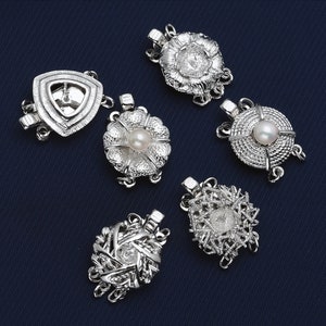 Puede incluir: Seis cierres de perla plateados para collares o pulseras. Cada cierre presenta un diseño diferente, incluyendo una flor, un triángulo y un círculo.