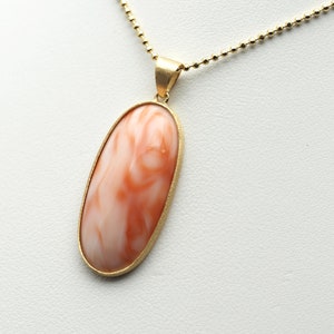 Puede incluir: Un collar de cadena de oro con un colgante que presenta una piedra de coral de forma ovalada grande con un patrón de remolino naranja y blanco.