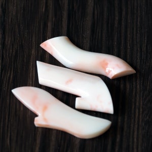 May include: Three pieces of coral in a light pink and white color. The coral is smooth and polished, and has a natural marbled pattern.