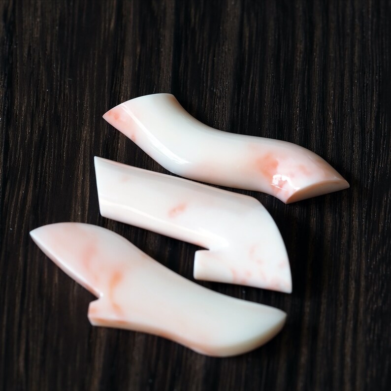 May include: Three pieces of coral in a light pink and white color. The coral is smooth and polished, and has a natural marbled pattern.