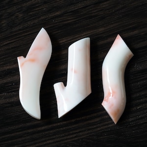May include: Three white ceramic molds with a pink marbled design. The molds are shaped like a high heel shoe, a vase, and a curved shape.