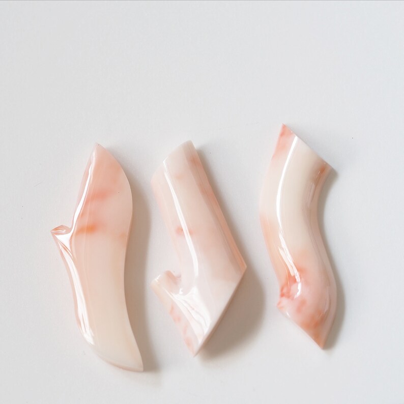 May include: Three pink and white marbled ceramic shoe-shaped ornaments. The ornaments are smooth and glossy.