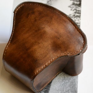 Könnte beinhalten: Eine braune Lederkamera-Hülle mit Nähten an den Rändern.