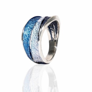 Op de afbeelding: Een zilveren ring met een blauw en wit emaille ontwerp. De ring is breed en heeft een gebogen vorm.