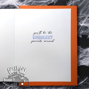 Puede incluir: Una tarjeta blanca con un borde naranja. La tarjeta tiene el texto "you'll be the GHOULEST parents around" escrito en negro con la palabra "GHOULEST" en morado.