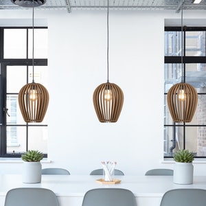 Peut inclure: Une table blanche avec six chaises grises et trois lampes suspendues en bois au-dessus. La table est installée dans un bureau moderne avec de grandes fenêtres.