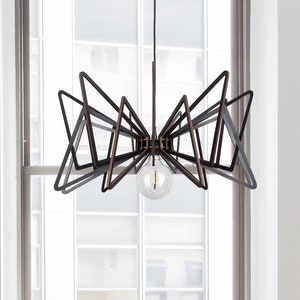 May include: A black and copper geometric chandelier with a single light bulb hanging from the ceiling in a room with a window and three chairs.