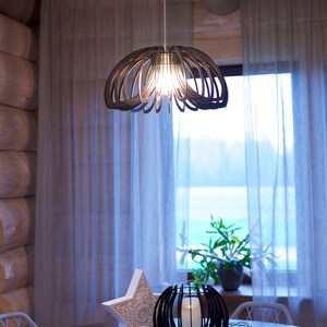 May include: A wooden table setting with a white star, a black candle holder, and a wooden pendant light hanging above. The table has a wooden surface and white placemats.