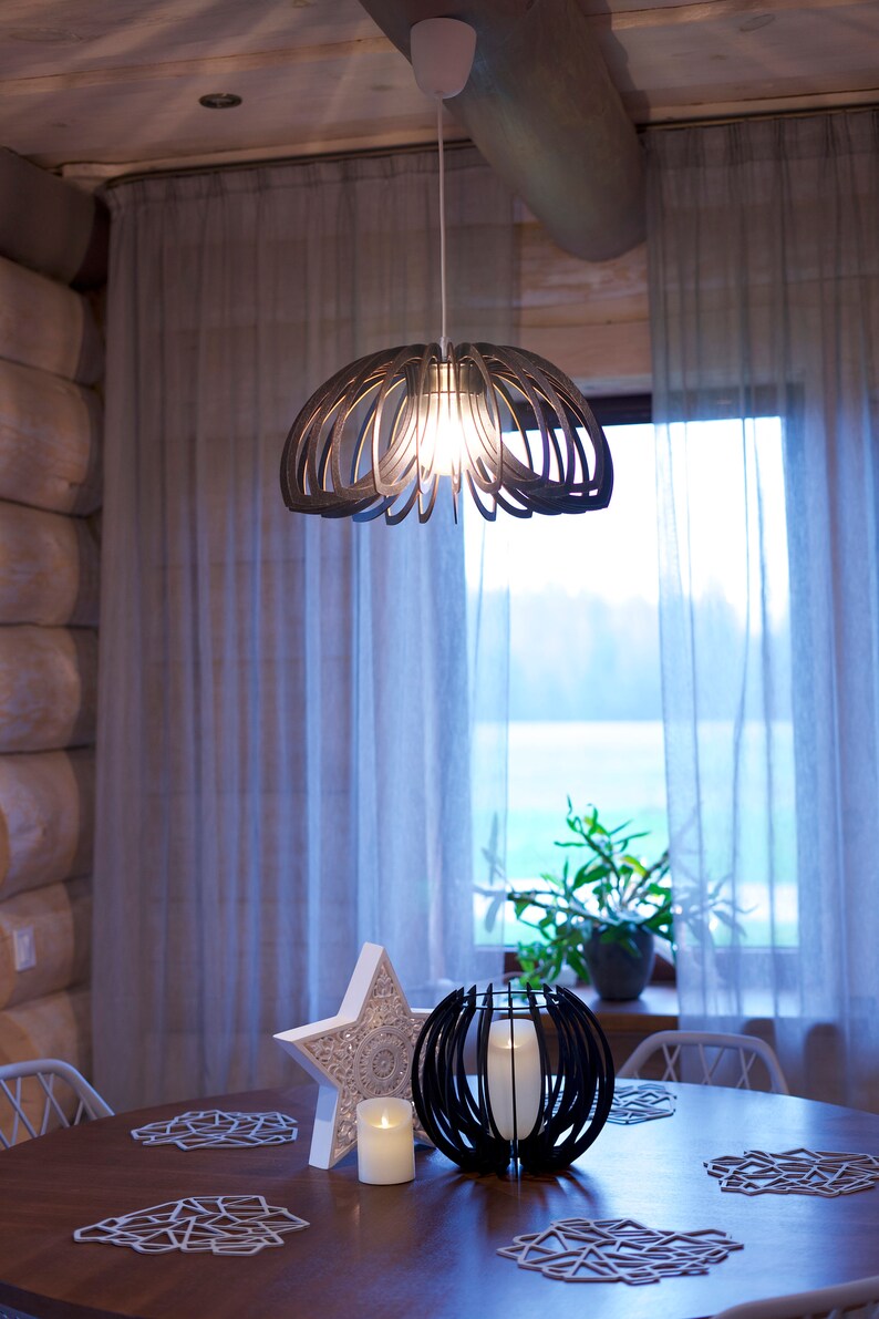 May include: A wooden table setting with a white star, a black candle holder, and a wooden pendant light hanging above. The table has a wooden surface and white placemats.