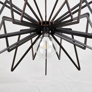 May include: A black metal ceiling light fixture with a geometric design. The light fixture has a clear glass globe with a light bulb inside.