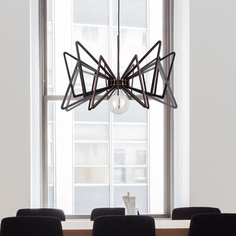 May include: A black and copper geometric chandelier with a single light bulb hanging from the ceiling in a room with a window and three chairs.