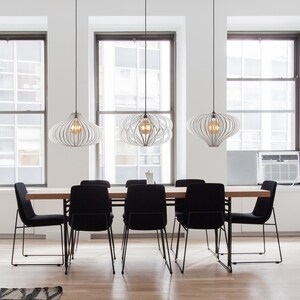Puede incluir: Una mesa de comedor con seis sillas negras y tres l&aacute;mparas colgantes blancas con una tapa de madera y patas de metal negro.
