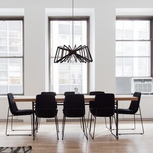 May include: A modern dining room with a black metal chandelier hanging over a wooden table with six black chairs. The room has large windows with white trim and white walls.
