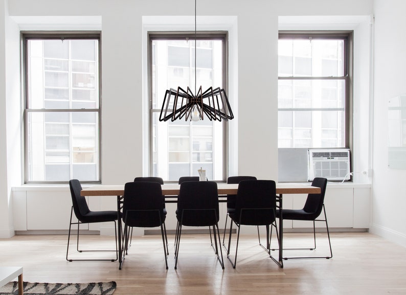 May include: A modern dining room with a black metal chandelier hanging over a wooden table with six black chairs. The room has large windows with white trim and white walls.