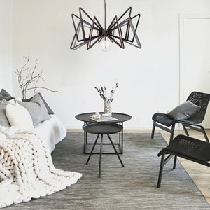 May include: A modern living room with a black geometric chandelier, a white couch with a chunky knit throw blanket, two black mesh chairs, and a set of black nesting coffee tables.