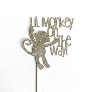 May include: Gold glitter cake topper with a monkey silhouette and the text "Lil monkey on the way".