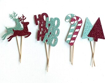May include: Set of six Christmas-themed cupcake toppers. The toppers are made of glitter paper and feature a reindeer, a candy cane, a Christmas tree, and the word "HO HO" repeated three times. The toppers are attached to wooden skewers.