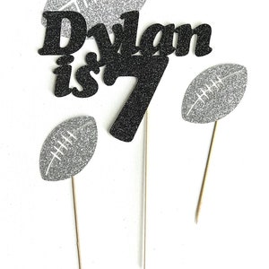 May include: Black and silver glitter cake topper with the name "Dylan is 7" and football designs.
