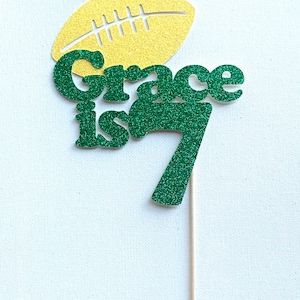May include: Green glitter cake topper with the text "Grace is 7" and a yellow glitter football.