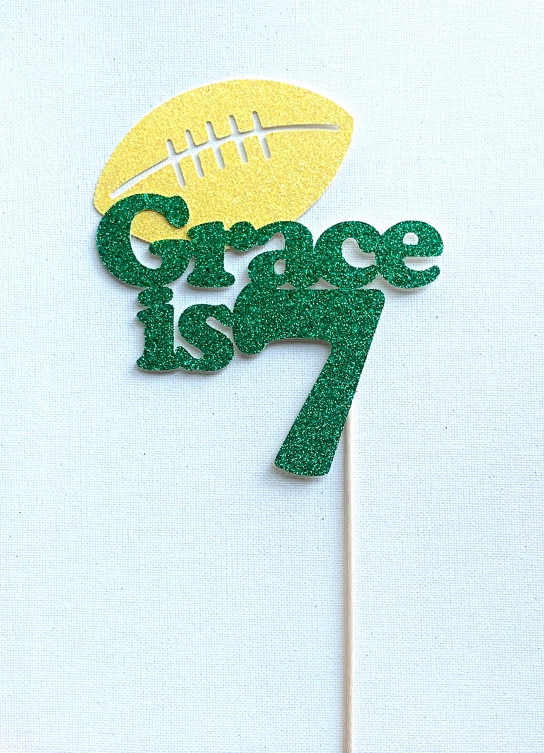 May include: Green glitter cake topper with the text "Grace is 7" and a yellow glitter football.