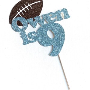May include: A blue glitter cake topper with the name "Owen is 9" and a brown glitter football.