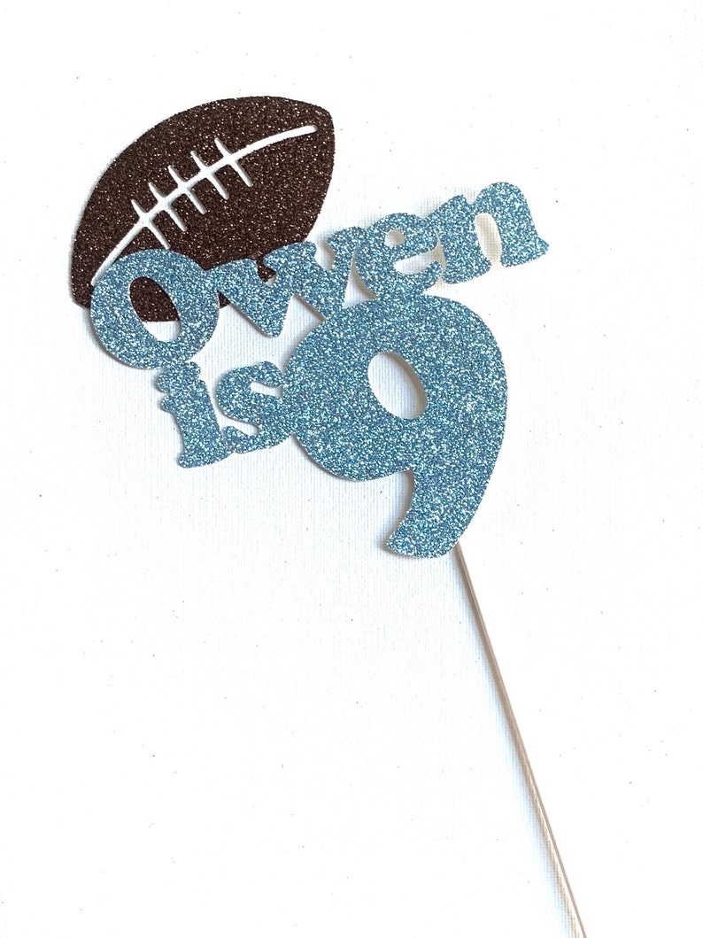 May include: A blue glitter cake topper with the name "Owen is 9" and a brown glitter football.