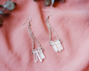 May include: Silver chain earrings with clear quartz crystal pendants. The earrings have a delicate, minimalist design.