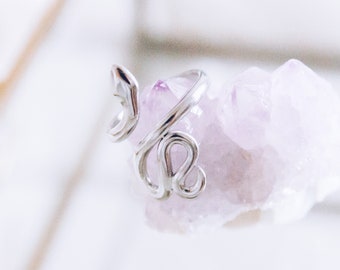 May include: Silver snake ring with a delicate, twisted design. The ring is displayed on a pink crystal.
