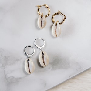 May include: Two pairs of earrings with shell charms. One pair has gold hoops and the other has silver hoops.