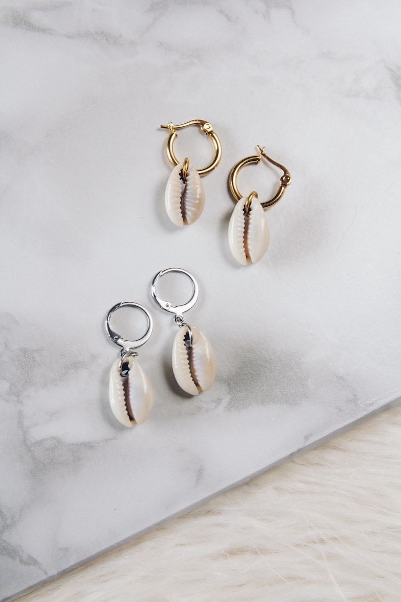 May include: Two pairs of earrings with shell charms. One pair has gold hoops and the other has silver hoops.