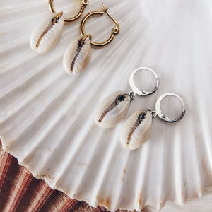 May include: Two pairs of earrings with shell charms. One pair has gold hoops and the other has silver hoops.