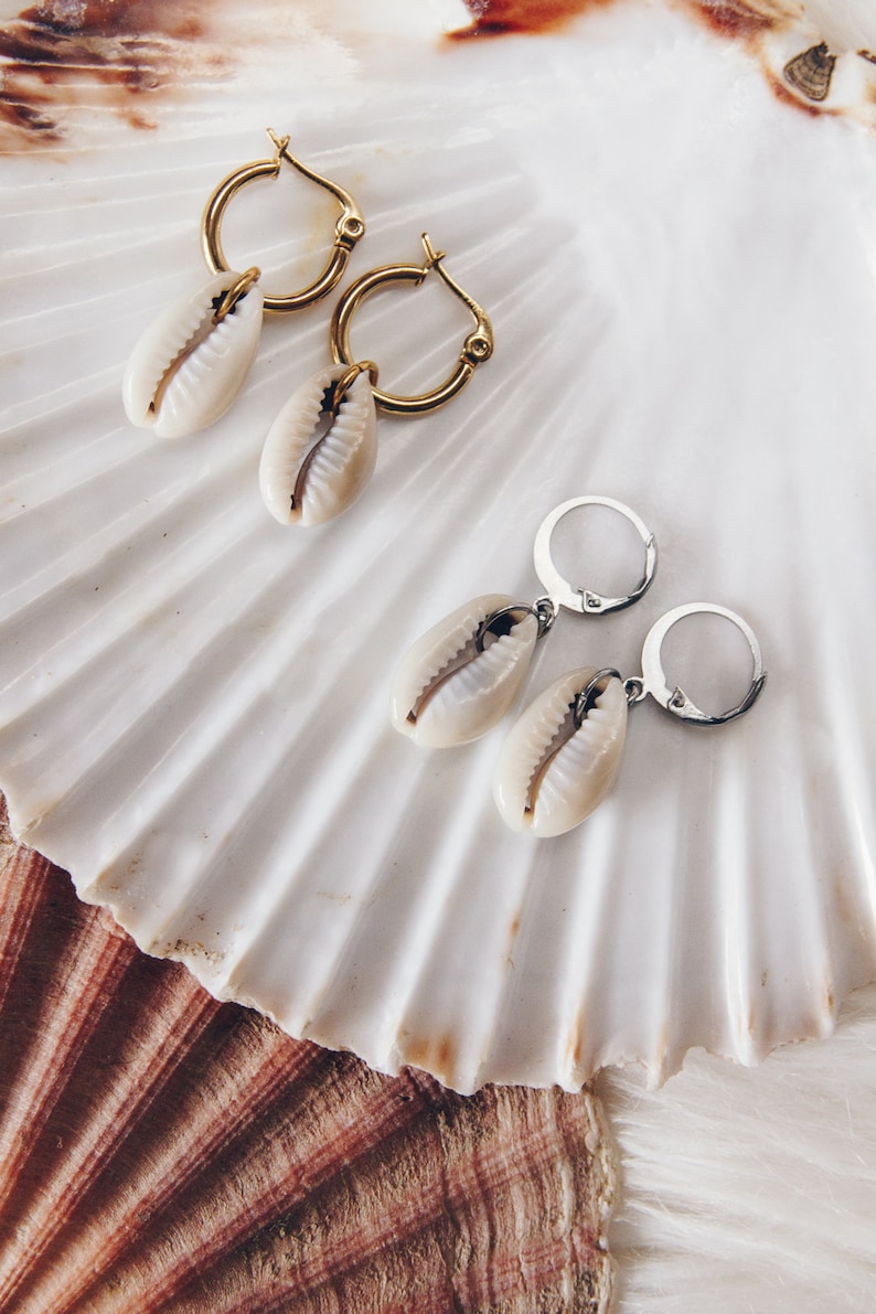 May include: Two pairs of earrings with shell charms. One pair has gold hoops and the other has silver hoops.