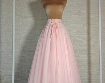 May include: A pale pink tulle skirt with a lace-up waistband and a bow tie. The skirt is on a white mannequin and is hanging on a white rack.