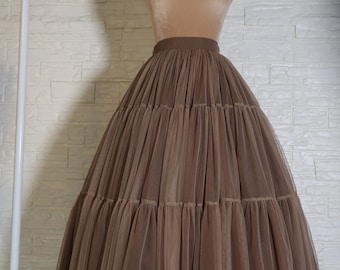 May include: A brown tulle skirt with multiple layers, displayed on a mannequin. The skirt has a wide waistband and a full, flowing silhouette. The fabric appears soft and lightweight, suitable for special occasions.
