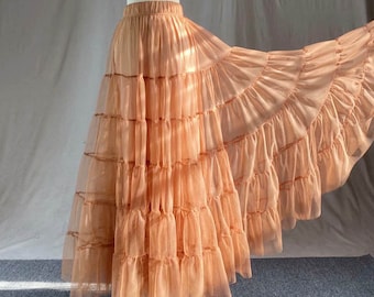 May include: A long, peach-colored tulle skirt with multiple layers of ruffles. The skirt is made of a soft, sheer fabric and has a flowy, romantic look.