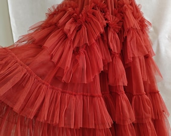 May include: A red tulle skirt with multiple layers of ruffles. The skirt is full and flowing, and it would be perfect for a special occasion.