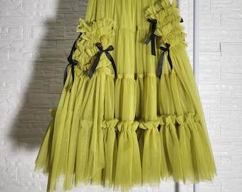 Peut inclure: Une jupe en tulle vert lime avec plusieurs couches et des nœuds en ruban noir sur les côtés. La jupe a un ourlet à volants.