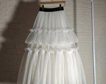 Peut inclure: Une jupe en tulle blanc avec une ceinture noire. La jupe est composée de plusieurs couches de tulle et est froncée à la taille.