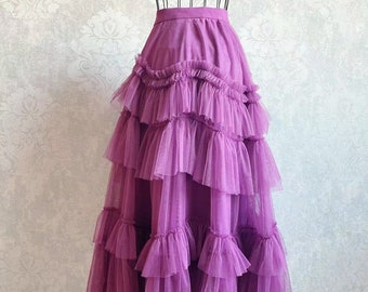 May include: A long, tiered skirt in shades of purple, displayed on a wire dress form. The skirt features multiple layers of ruffled tulle, creating a voluminous and flowing silhouette. The waistline is a solid, darker purple.
