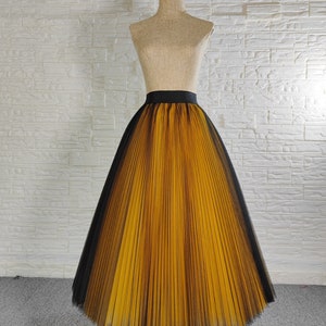 May include: A long, yellow and black tulle skirt with pleats. The skirt has a black waistband and is on a mannequin.