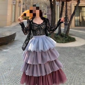 May include: A layered tulle skirt in shades of lavender and mauve, paired with a black lace top and jacket. The outfit is completed with black heels. The ensemble is suitable for special occasions.