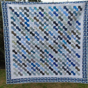 May include: A blue and white patchwork quilt with a bow tie pattern. The quilt is made of various shades of blue and white fabrics and is bordered with a blue and white scalloped trim.