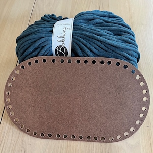 May include: A teal blue cotton rope yarn ball with a white label that says "Bobbiny" and "Jumbo String". A brown oval-shaped base with holes around the edge.