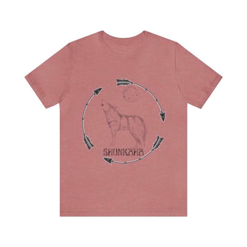 Puede incluir: Una camiseta de color rojo heather con una ilustraci&oacute;n en blanco y negro de un lobo aullando a la luna. El lobo est&aacute; rodeado por un c&iacute;rculo de flechas y la palabra "SHUNKARA" est&aacute; escrita debajo del lobo.