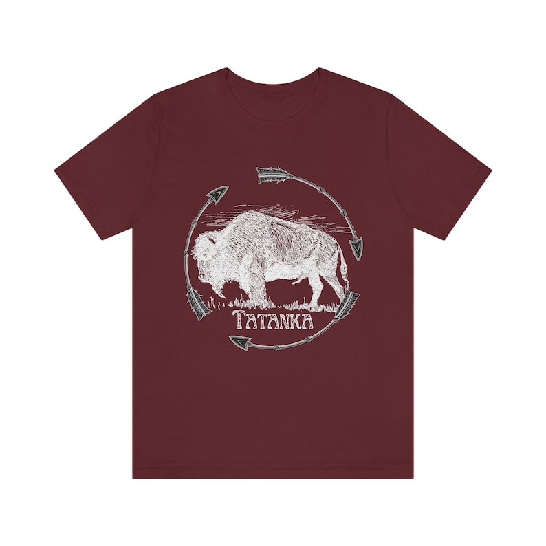 Pu&ograve; includere: Una t-shirt color granata con una grafica bianca di un bufalo circondato da frecce. Il testo "Tatanka" &egrave; stampato sotto il bufalo.