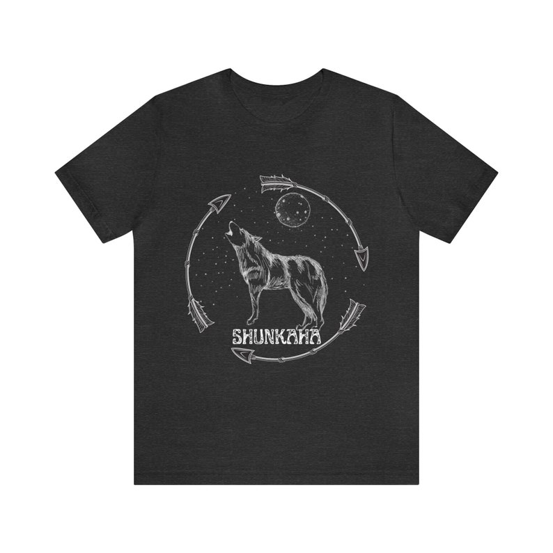 Puede incluir: Una camiseta gris oscuro jaspeada con un gr&aacute;fico blanco de un lobo aullando a la luna. El lobo est&aacute; rodeado de flechas y el texto "SHUNKAHA" est&aacute; debajo del lobo.