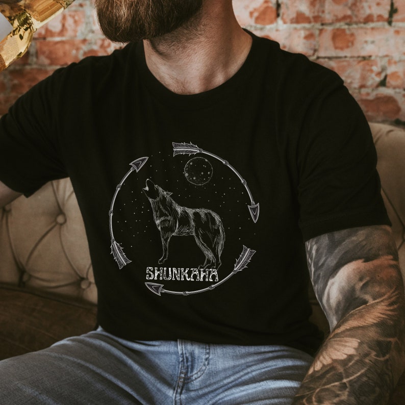 Puede incluir: Una camiseta negra con un lobo blanco aullando a la luna. El gr&aacute;fico tambi&eacute;n incluye flechas y el texto "Shunkara".