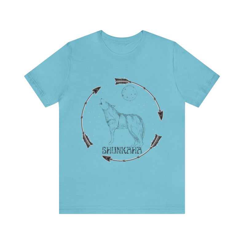 Puede incluir: Una camiseta azul claro con un gr&aacute;fico de un lobo aullando a la luna. El lobo est&aacute; rodeado por un c&iacute;rculo de flechas y la palabra "Shunkara" est&aacute; impresa debajo del lobo.